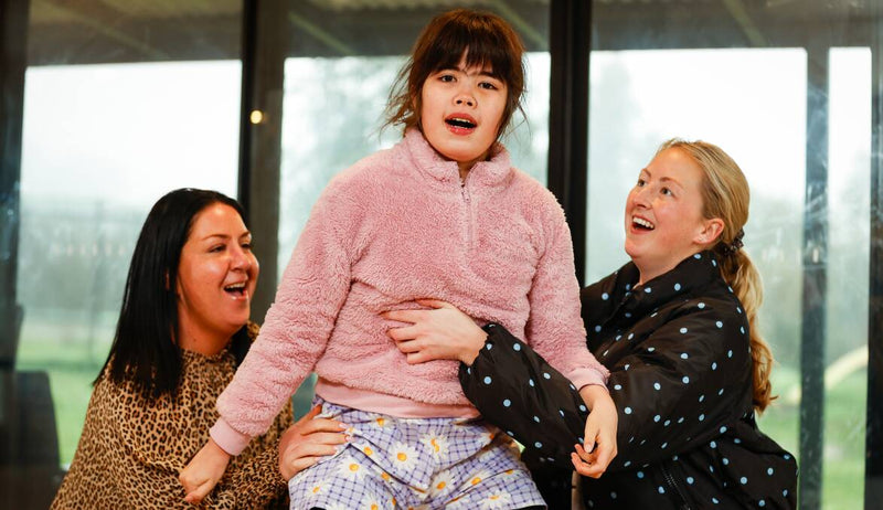 Three happy individuals support a girl wearing cozy attire, representing Steps For Skye charity merchandise for Sanfilippo research.