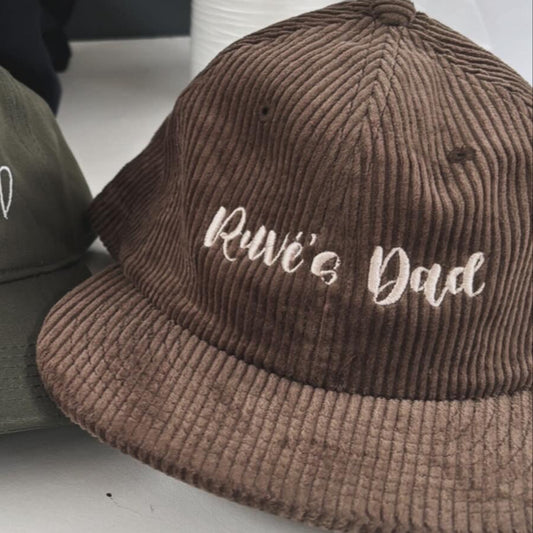 Two caps, one green and one brown, with embroidered text on a white surface.