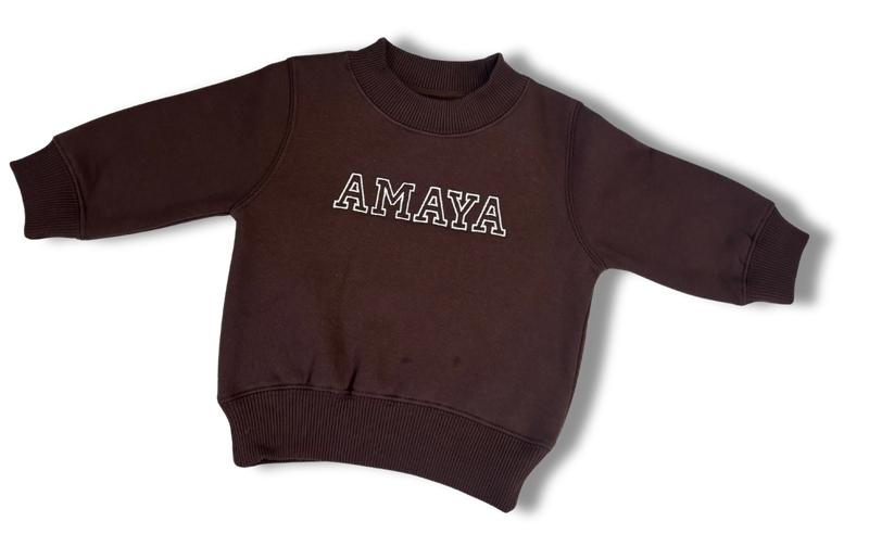 A dark brown long-sleeve crewneck sweatshirt with 'AMAYA' embroidered across the chest in white outlined block letters, displayed on a clean white background.