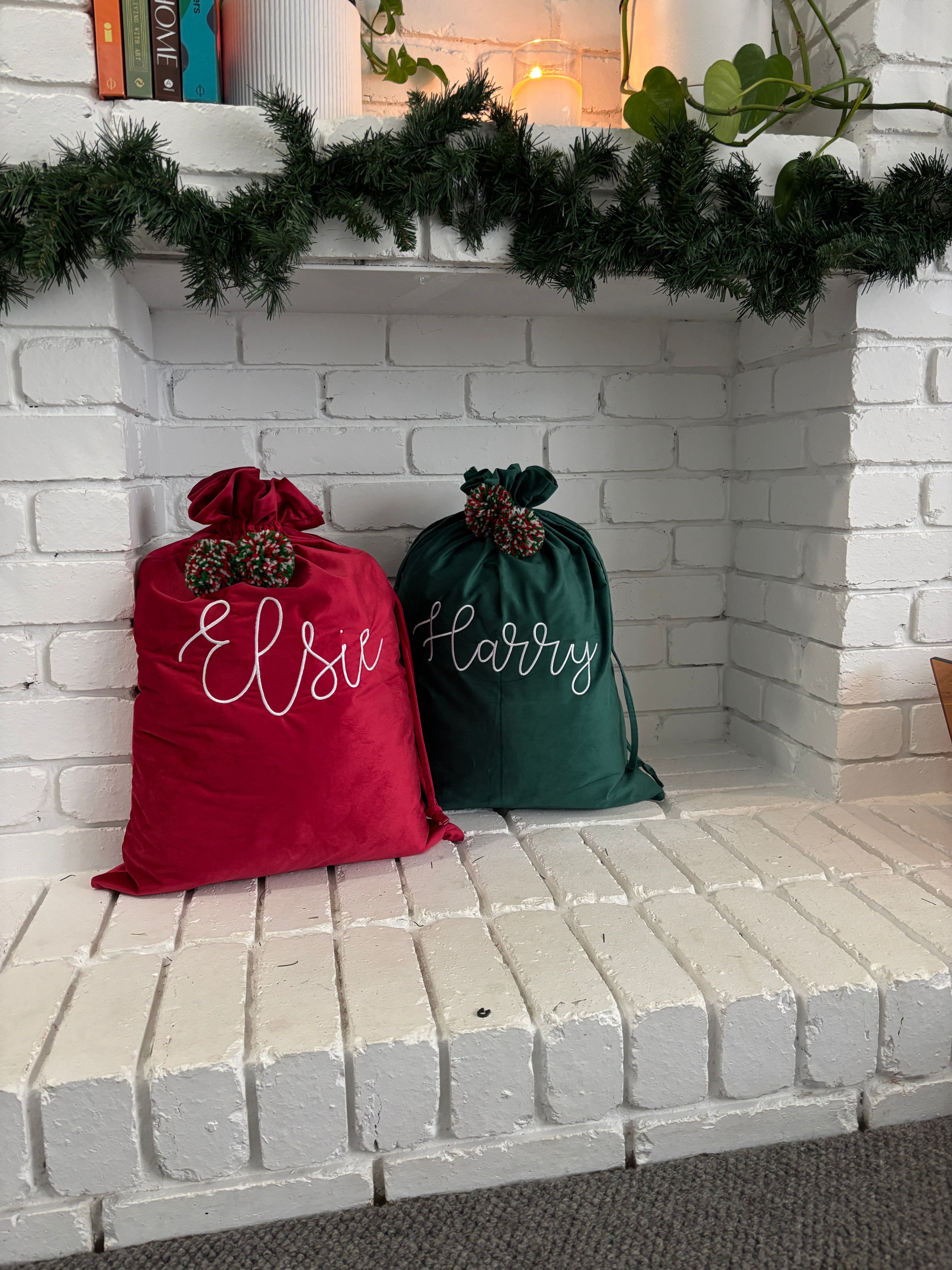 Pom Pom santa sacks with names on a white brick wall  fireplace with Christmas decorations.