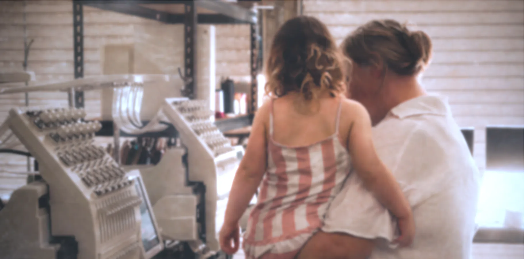 mother and child standing together in a room with embroidery machines.