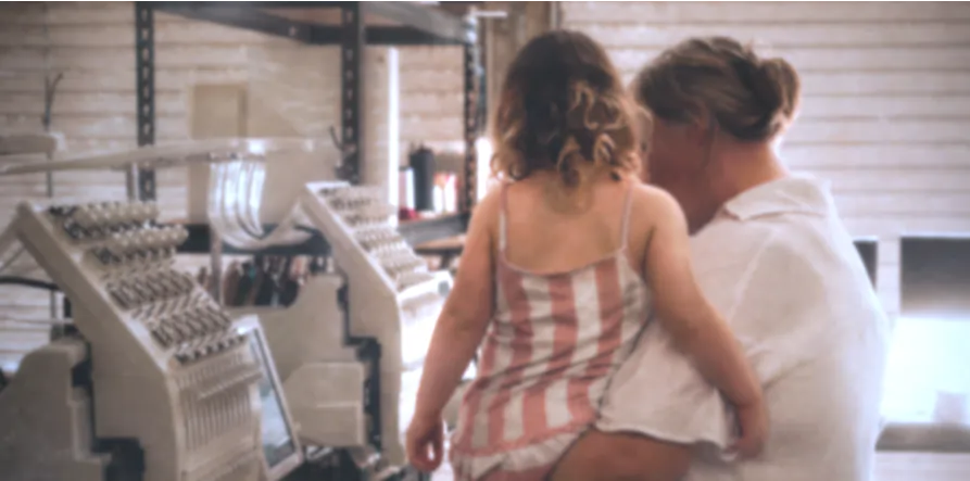 Two people standing together in a room with embroidery machines.