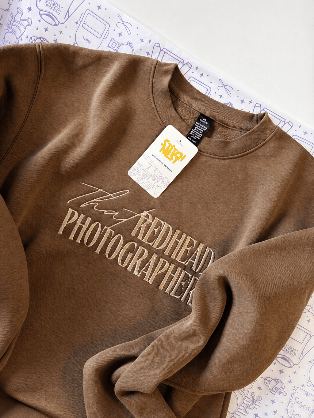 Personalized embroidered sweatshirt in walnut color with stylish text design and tag on a white background.