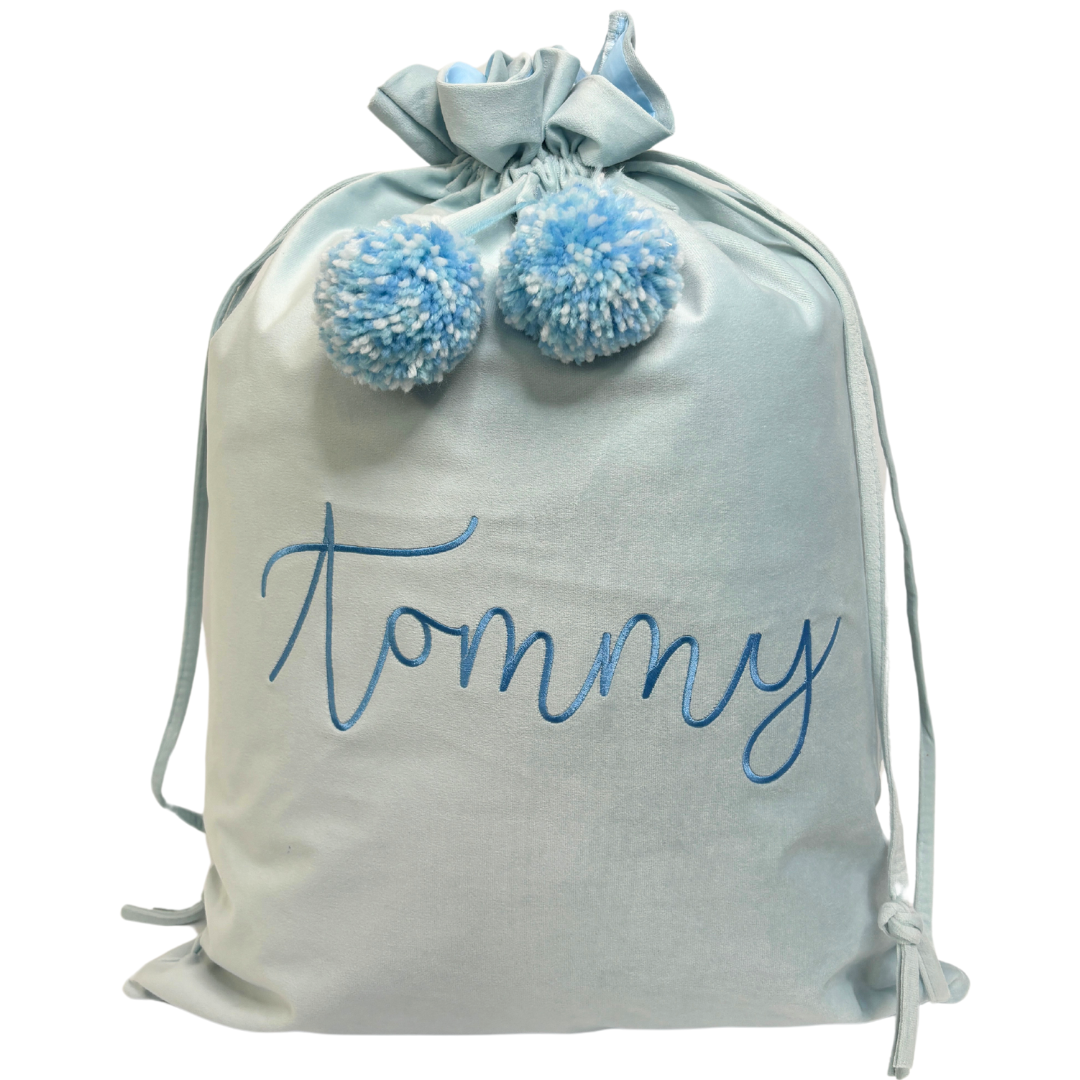 Personalised pale blue velvet Santa sack with blue embroidered name ‘Tommy’ and soft light blue pom poms